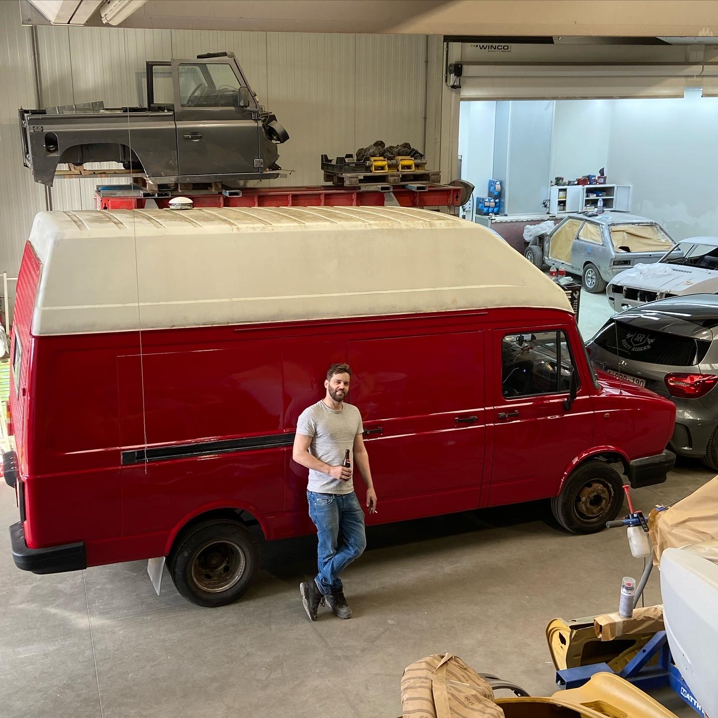 Koen, camperbouwer bij Reisnest, voor een rode campervan in zijn werkplaats in Mechelen